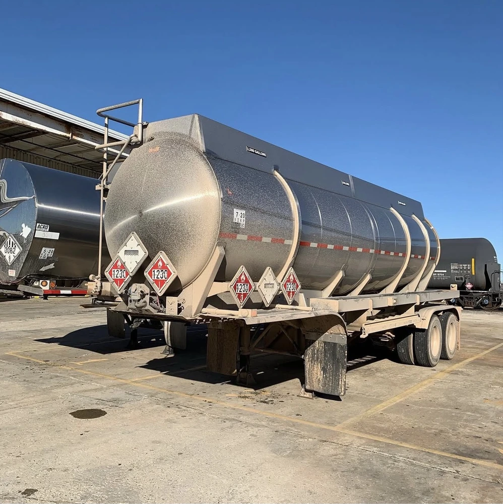 Before washing: a tanker trailer with visible dirt covering its tank, frame, and wheels.